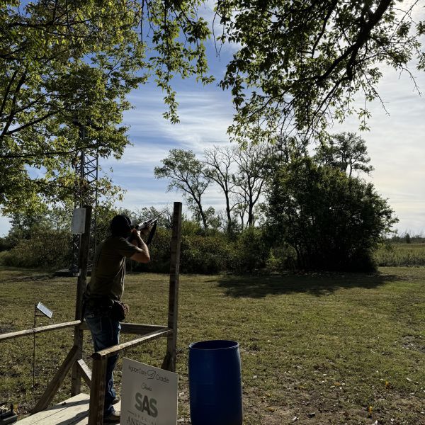 Person_standing_ready_for_clay_at_edge_of_grassy_field_with_trees