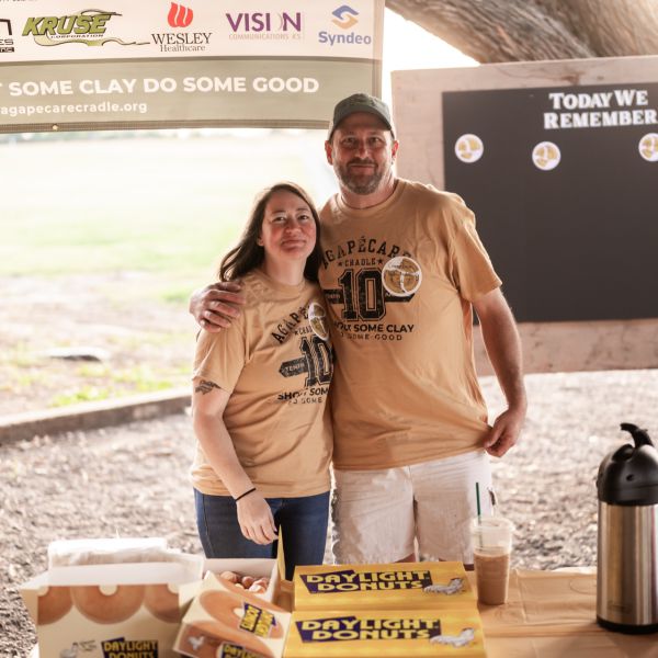 Couple_at_outdoor_event_embracing_behind_table_with_drinks_and_pastries