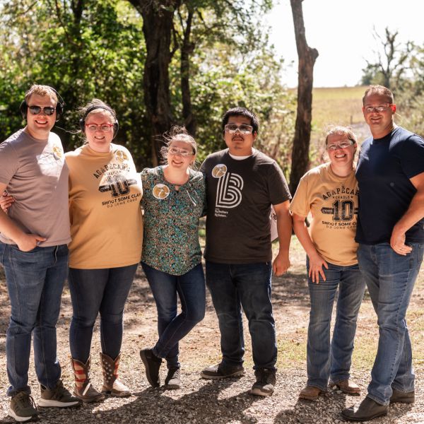 Group_of_six_people_standing_together_outdoors_with_trees_behind_them