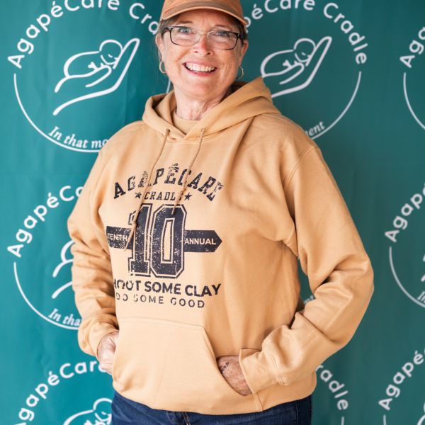 Older_woman_wearing_yellow_sweatshirt_with_text_standing_behind_signage