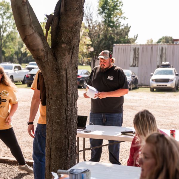 Outdoor_gathering_of_people_standing_near_picnic_tables_with_man
