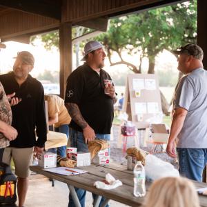 Group_of_men_gathered_at_picnic_tables_talking_at_sscdsg_event